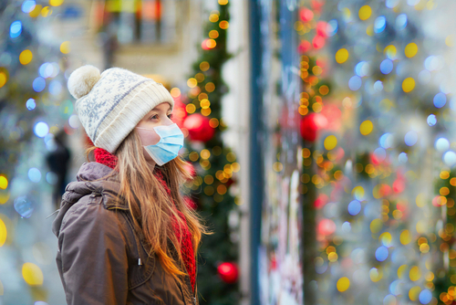 Young woman outside with a mask on with Christmas lights in the background. She is beating the holiday blues by getting out while social distancing.
