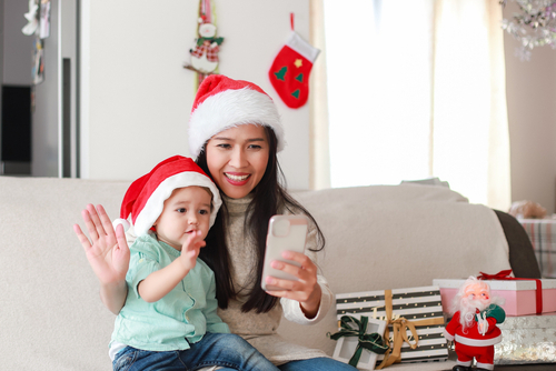 Young woman helping her young son to handle holiday stress better during the pandemic. The mom and her son are interacting over her i-phone with relatives during the holidays.